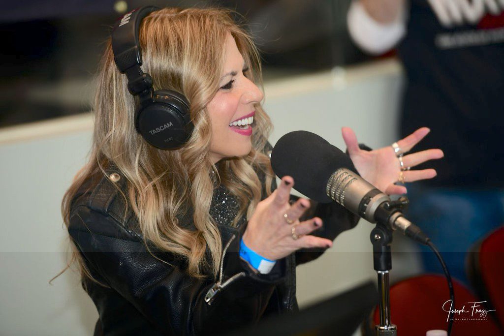 Woman enthusiastically speaking into a microphone during a broadcast.