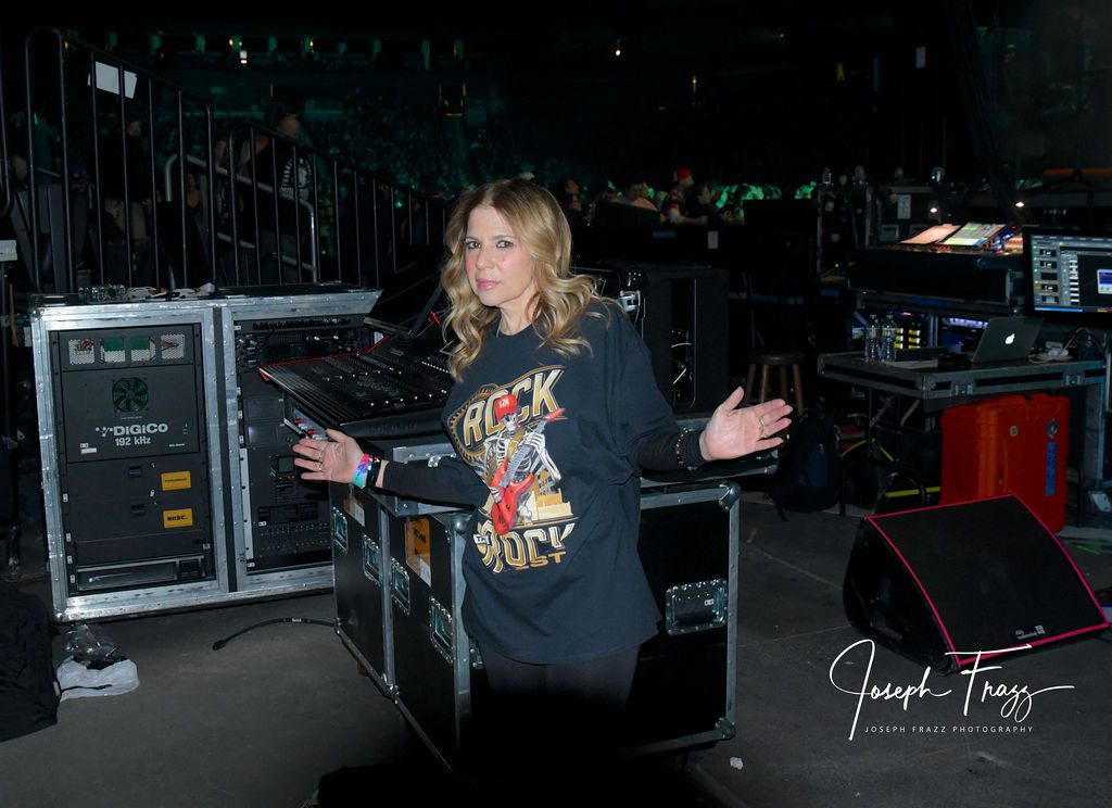 Person wearing a graphic hoodie standing with arms spread in a backstage area.