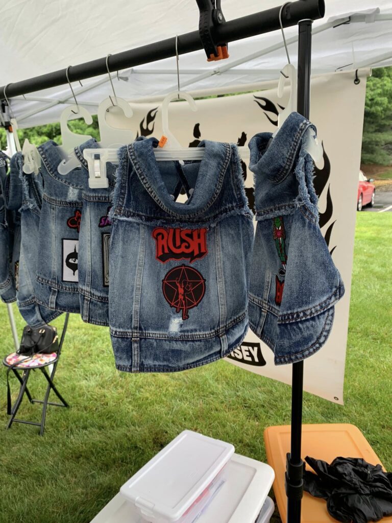 Denim dog jackets with patches hanging at an outdoor market.