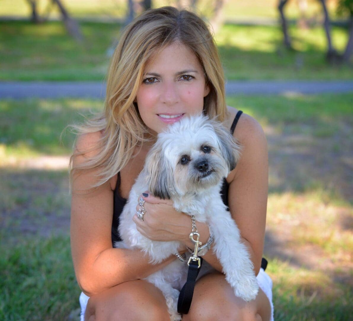 Woman happily holding a small white dog outdoors.
