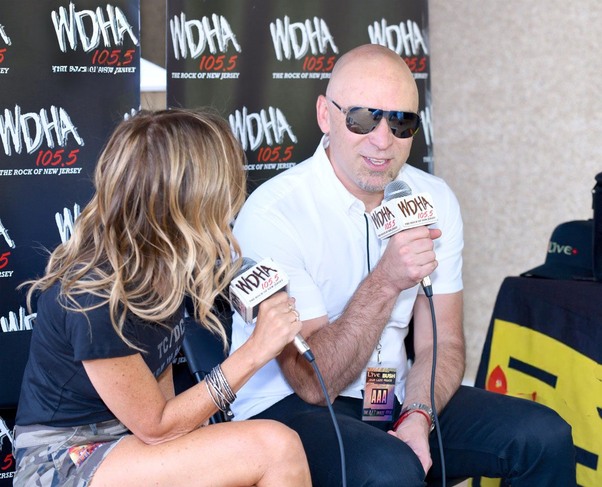 Two people with microphones conducting an interview at a radio station booth.