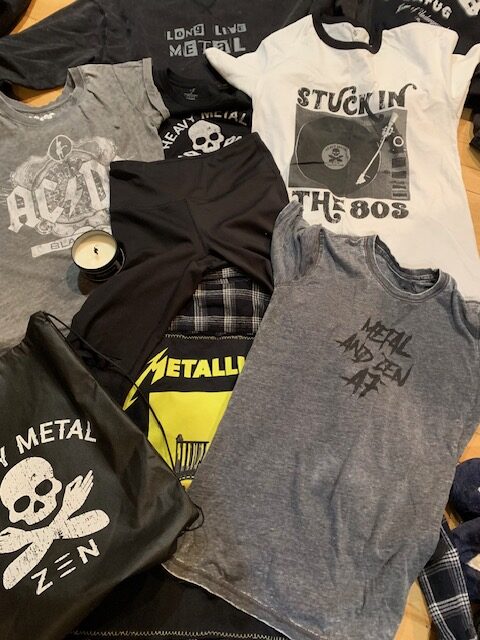 A collection of rock band t-shirts and casual wear laid out on a bed.