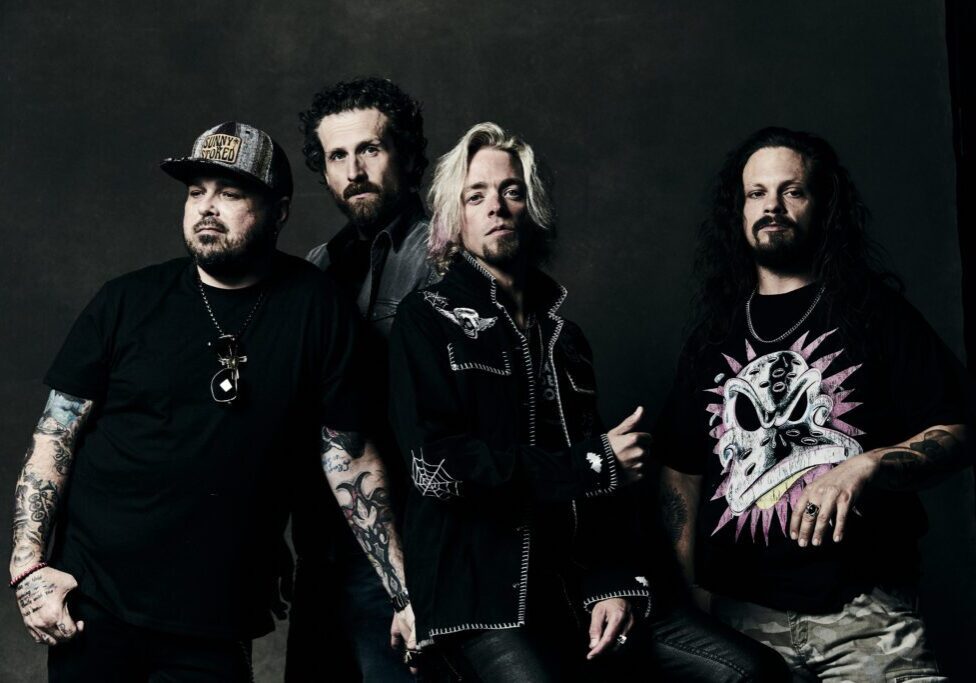 Four men with diverse styles posing in dark, edgy attire against a dark background.